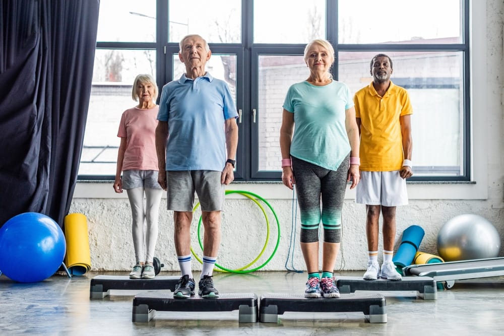 multiethnic,senior,athletes,synchronous,exercising,on,step,platforms,at,gym