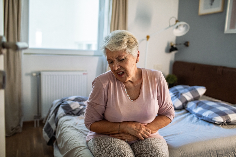 senior,woman,in,pain,holding,stomach,on,bed,at,home