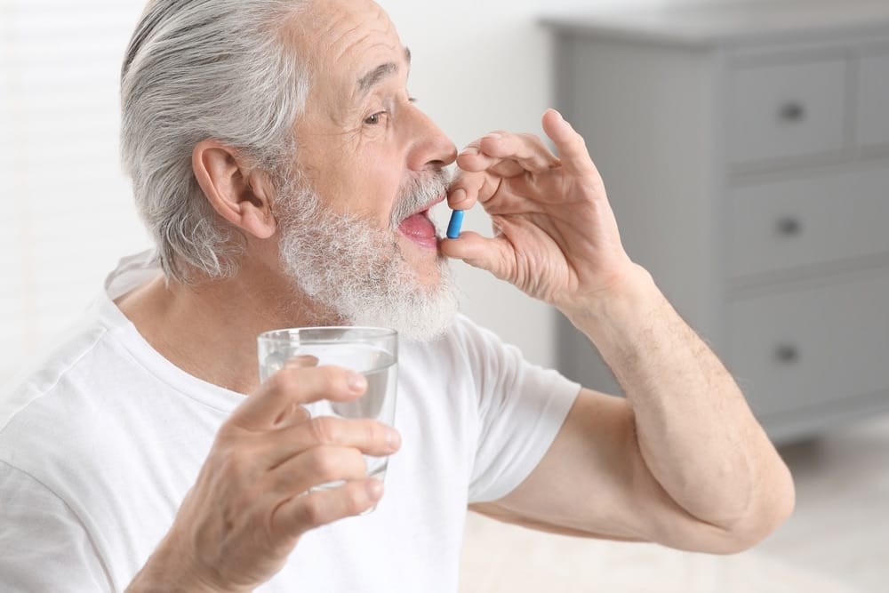 senior,man,with,glass,of,water,taking,pill,indoors