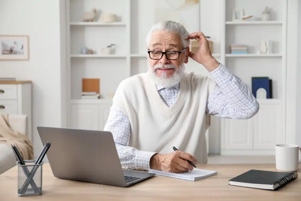 senior,man,taking,notes,while,learning,online,at,desk,indoors.