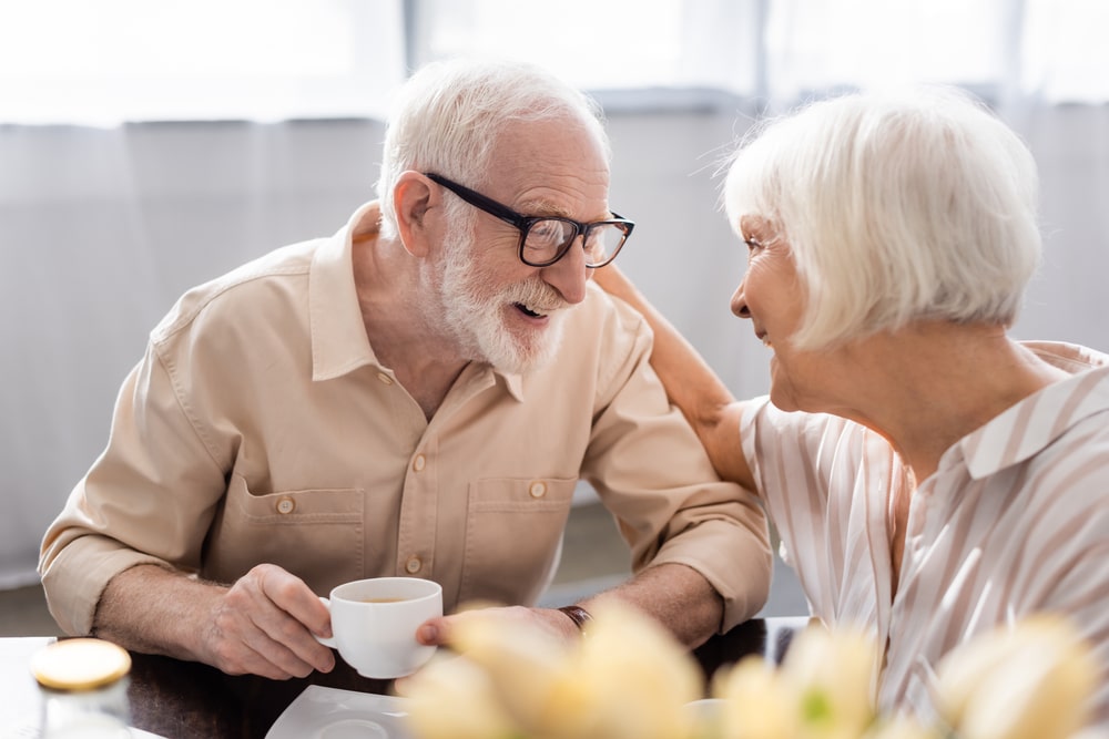 selective,focus,of,positive,senior,woman,embracing,husband,with,cup