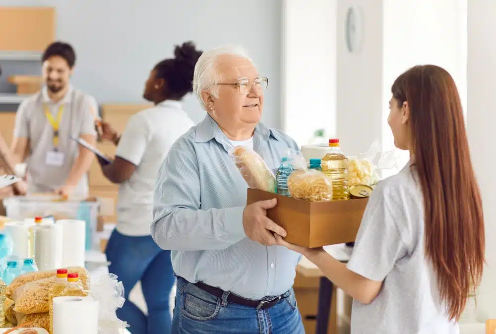 volunteer,gives,a,box,of,food,to,an,elderly,male