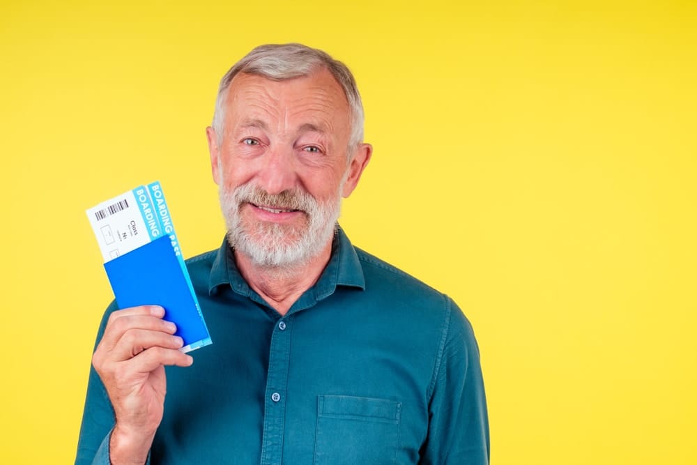smiling,senior,man,holding,passport,in,blue,cover,and,tickets