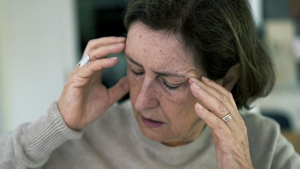senior,woman,in,visible,distress,,holding,head,with,eyes,closed,