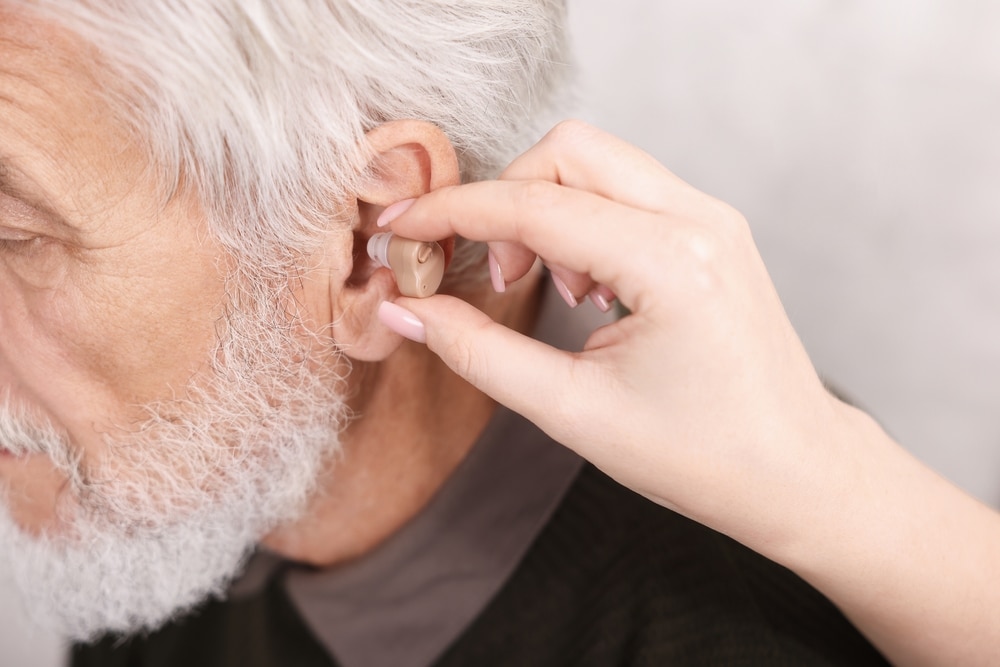 caregiver,helping,senior,man,to,put,in,hearing,aid,at