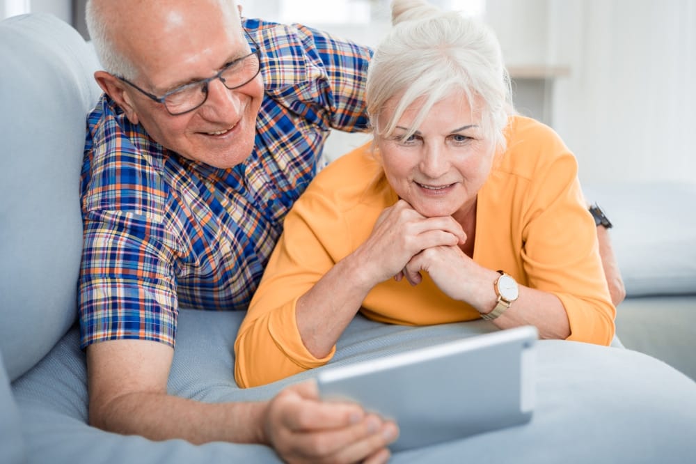 happy,senior,couple,looking,at,tablet,lying,on,sofa,at