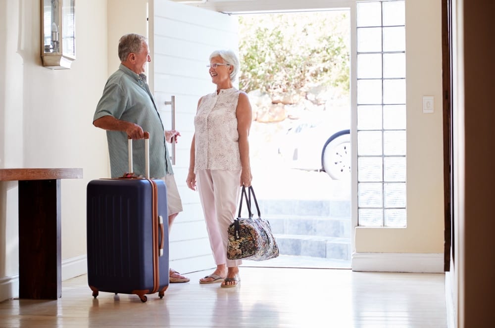 senior,couple,standing,by,front,door,with,suitcase,about,to
