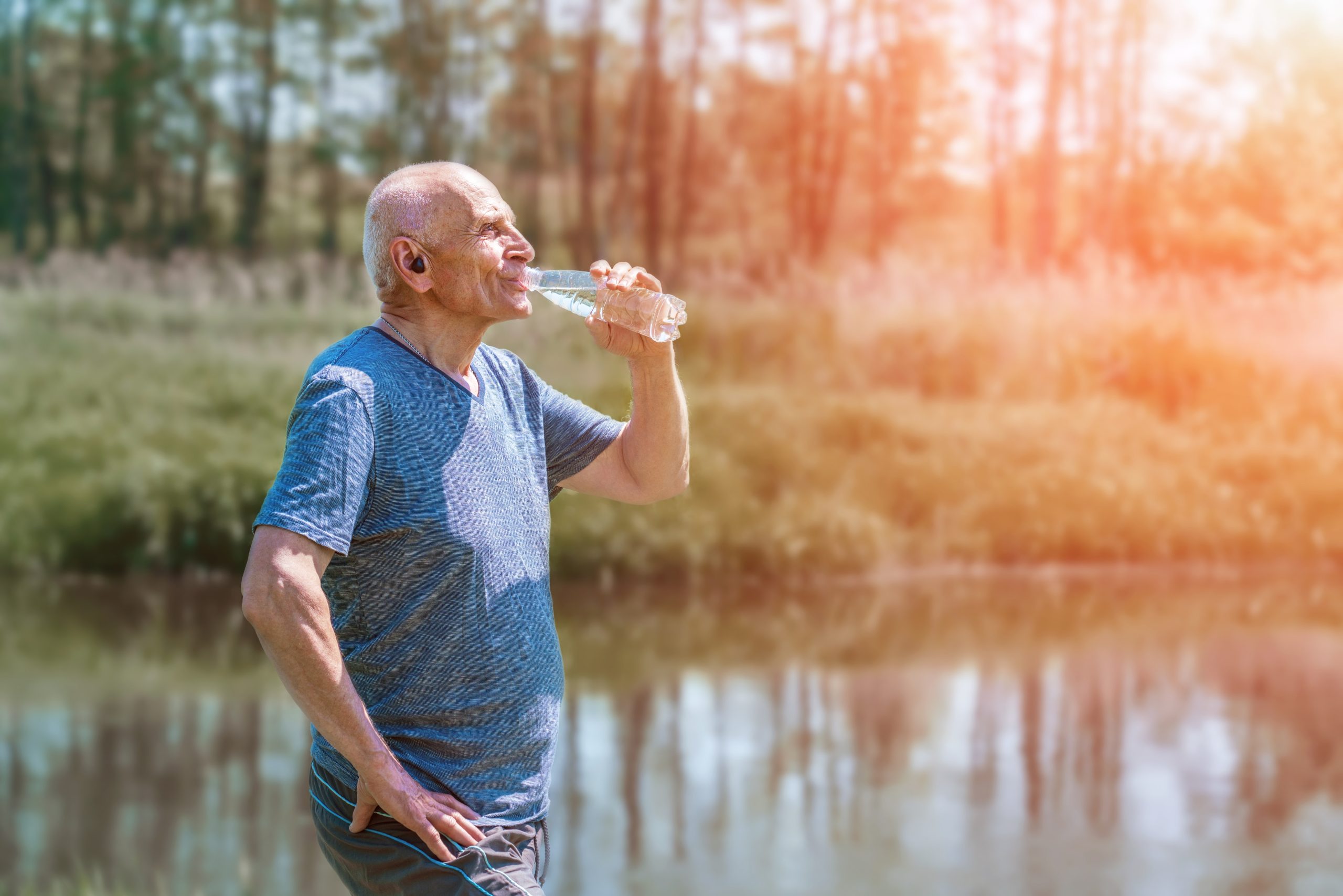 elder,man,in,headphones,in,ears,drinking,water,from,plastic