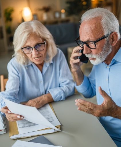 senior,couple,looking,at,documents,and,making,a,stressful,phone